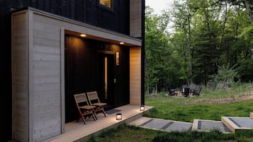 A modern house with a wooden exterior, a porch with two chairs, and a number sign.