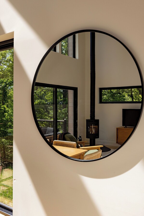 A circular mirror reflecting a room with a fireplace, a sofa, and a television. - NEW Modern Nordic Cabin Near Shenandoah National Park w/ Hot Tub + EV Charger (Rileyville)