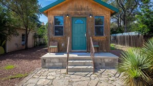 Una pequeña cabaña de madera con puerta verde, dos ventanas y un porche con un banco.
