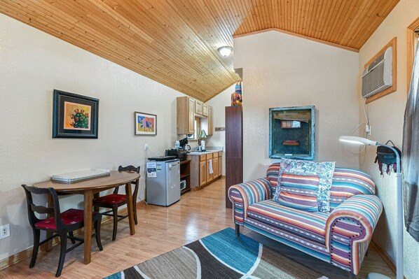 A cozy living room with a striped sofa, a dining table with chairs, a kitchenette, and a wooden ceiling. - Lizzy`s Place - Cute, tiny house (Alpine)