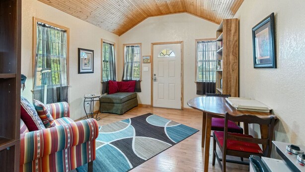 Una habitación acogedora con techo de madera, un sofá con cojines coloridos, una pequeña mesa y una puerta con un vitral.