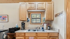 Una cocina con armarios de madera, una ventana, un lavamanos, una cafetera y varios utensilios de cocina.