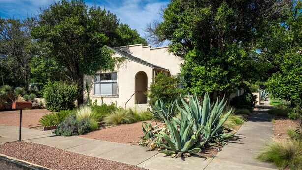 Um edifício com fachada em estuque, entrada em arco e um jardim com plantas de agave.