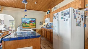 Uma cozinha com armários de madeira, uma ilha revestida de azulejos, uma geladeira com imãs e um quadro na parede.