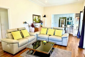 A living room with a sectional sofa, a coffee table, and a kitchen area in the background. - Four Season Home (Bentleigh)