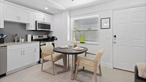 A modern kitchen with white cabinets, a black countertop, and a dining area with two chairs and a round table. - Cozy 1BR w/ Pool · 4 min from Siesta (Sarasota)