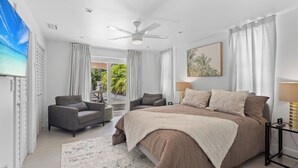 A bedroom with a large bed, two armchairs, a ceiling fan, and a TV. - Cozy 1BR w/ Pool · 4 min from Siesta (Sarasota)