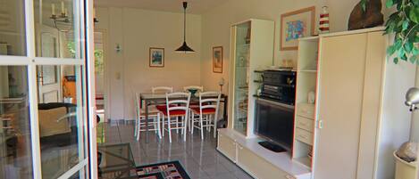 Una sala de estar moderna con comedor, muebles blancos y una vitrina de vidrio.