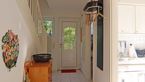 A hallway with a wooden bench, a decorative wall piece, a door with a window, and a kitchen area with cabinets and a countertop.