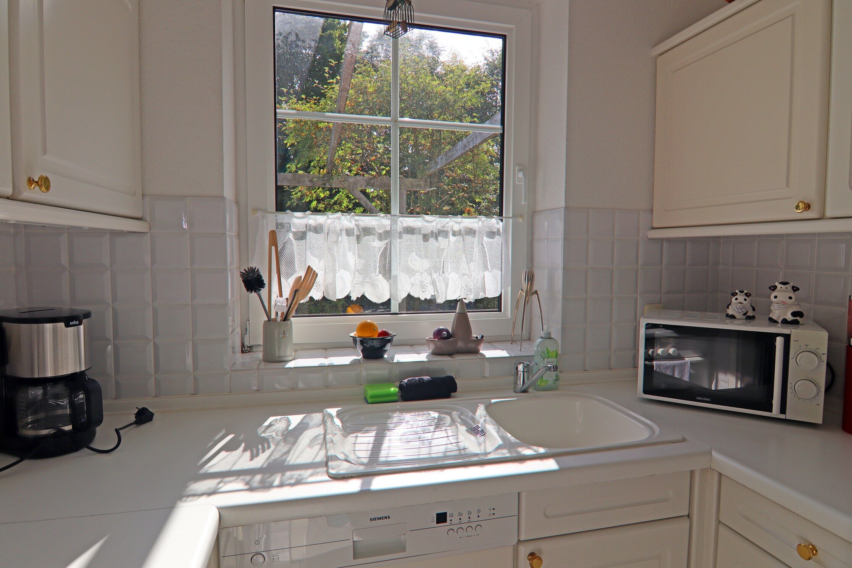 A kitchen with a window, white cabinets, a sink, a microwave, and a coffee maker.