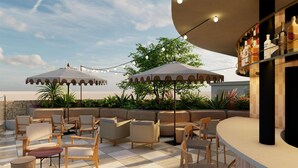 An outdoor seating area with cushioned chairs and tables, surrounded by greenery and umbrellas, with a bar area visible to the right. - Hyatt Centric Queretaro (Querétaro)