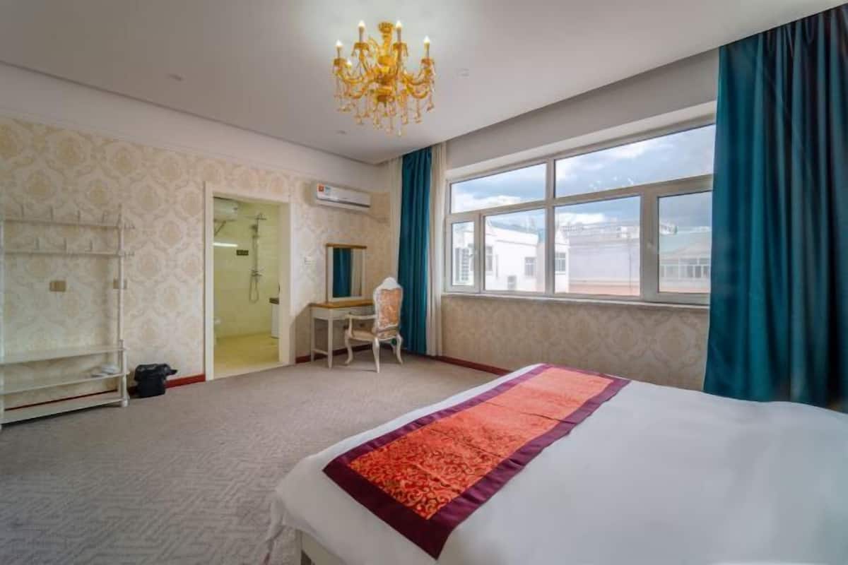 Quarto de hotel com cama, escrivaninha, cadeira, lustre e uma grande janela.