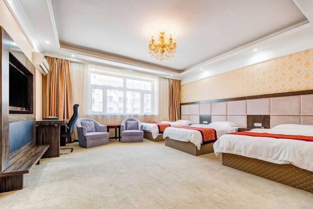 Quarto de hotel com três camas, televisão, lustre e uma janela grande.