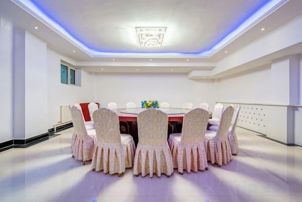 Une salle de conférence avec une table ronde et des chaises, un luminaire au plafond et un mur blanc.