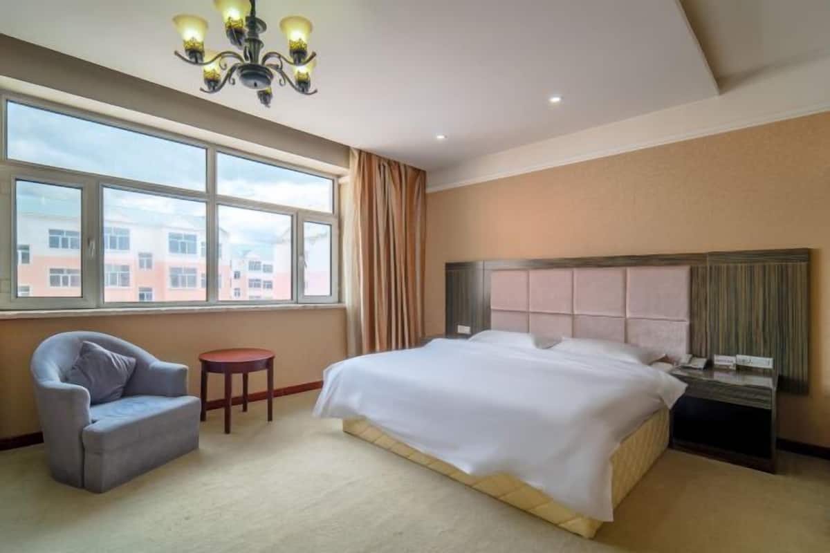 Quarto de hotel com uma cama grande, uma cadeira, uma mesinha e um candelabro.