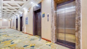 Un pasillo de hotel con alfombra estampada, puertas de madera y un ascensor.