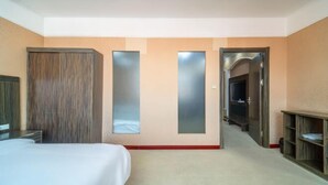 Habitación de hotel con cama, armario, espejo y puerta que da a un pasillo.