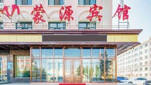 Entrada de un hotel con fachada de vidrio, alfombra roja que lleva a las puertas y un cartel con caracteres chinos.