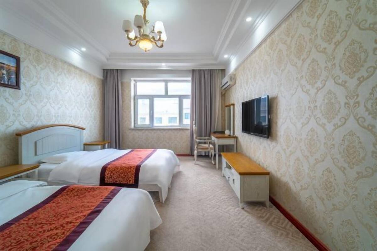 Quarto de hotel com duas camas, uma escrivaninha, uma cadeira, uma televisão e uma janela com cortinas.