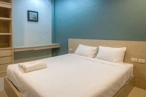 A neatly made bed with white linens, a wooden headboard, and a small bedside table with a white towel. - Hop On Phuket (Phuket)