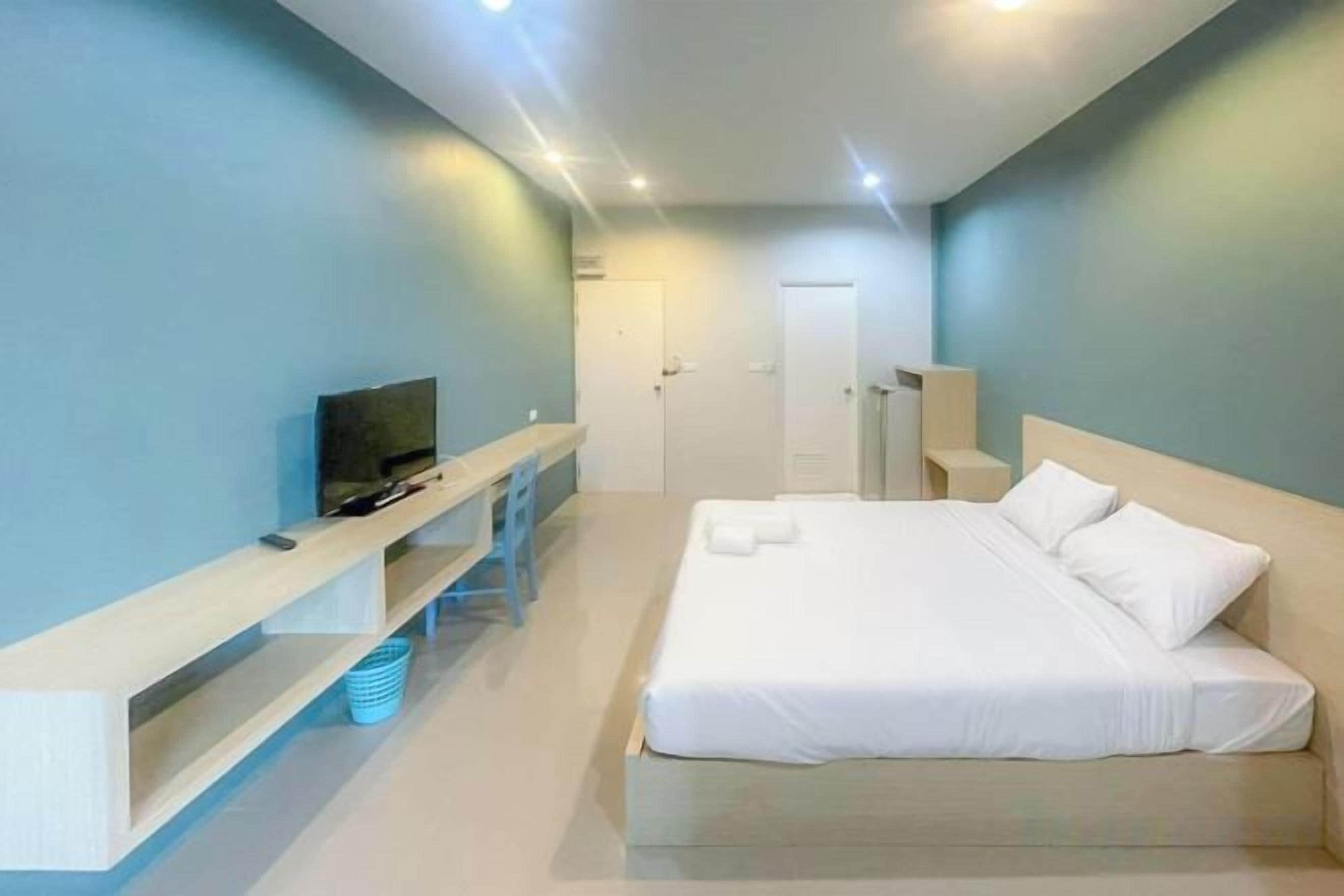 A bedroom with a bed, a TV, a desk, and a door.