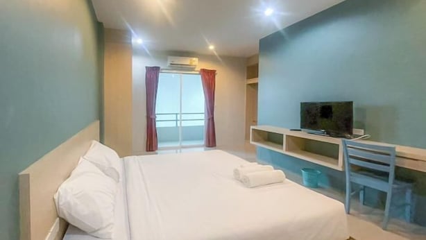 Une chambre d’hôtel avec un lit, un téléviseur posé sur un meuble, un bureau et une fenêtre avec des rideaux.