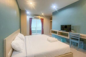 A hotel room with a bed, a TV on a stand, a desk, and a window with curtains. - Hop On Phuket (Phuket)