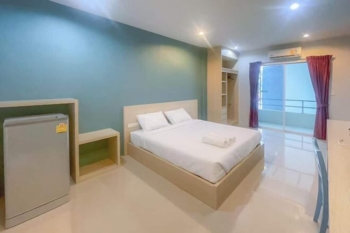 A bedroom with a bed, a small table, a wardrobe, and an air conditioning unit.