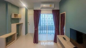 Une pièce aux murs de couleur turquoise, avec un meuble TV en bois, un téléviseur à écran plat, une télécommande et un appareil de climatisation.