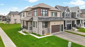 A two-story residential building with a garage, a covered front porch, and a well-maintained lawn. - Niagara Getaway: 4 BDR• Mins from Falls & Wineries (Thorold)