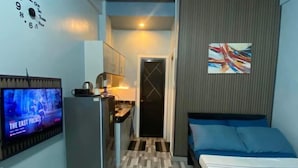 A compact hotel room with a kitchenette, a bed with blue bedding, a television on the left, and a painting on the wall. - Amplayo Apartelle Studio Type Unit (Cagayan De Oro)