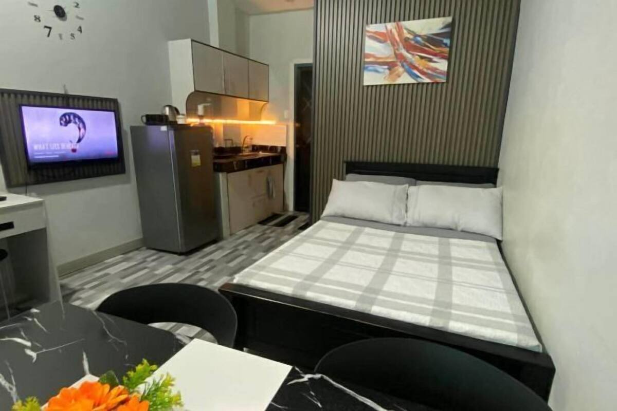 A compact hotel room with a bed, a desk, a small kitchenette, and a TV.