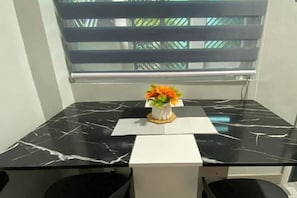 A small table with a black marble top, a white vase with orange flowers, and a white placemat. - Amplayo Apartelle Studio Type Unit (Cagayan De Oro)