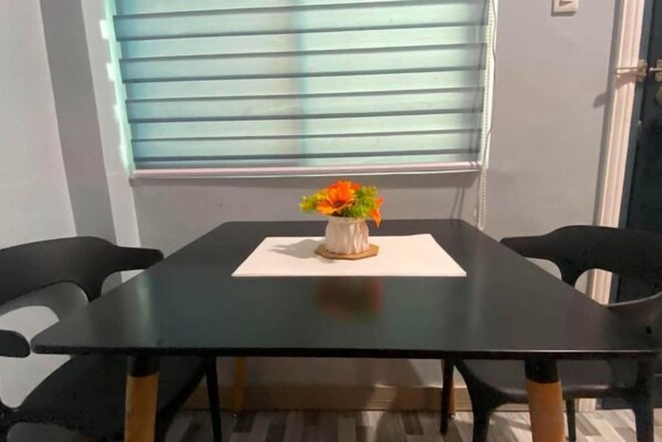 Et spisebord med stole, en vase med blomster og et vindue med persienner.