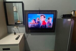A television mounted on a wall with a remote control on a white surface below. - Amplayo Apartelle Studio Type Unit (Cagayan De Oro)