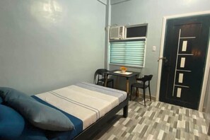 A small room with a bed, a desk, a chair, and a door. - Amplayo Apartelle Studio Type Unit (Cagayan De Oro)