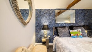 A bedroom with a large bed, a nightstand, a lamp, a mirror, and a tufted chair. - Charming guesthouse for two with private parking and en-suite (North Yorkshire)