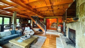 A spacious living room with a stone fireplace, wooden ceiling beams, and a staircase leading to an upper level. - Blue Ridge Mountain Retreat (Fannin County)