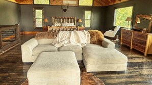 A spacious room with a large sectional sofa, a bed with a wooden headboard, and a wooden ceiling. - Blue Ridge Mountain Retreat (Fannin County)