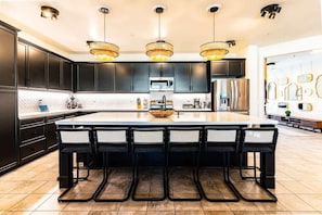 Uma cozinha moderna com armários escuros, uma ilha central com banquetas e iluminação pendente.