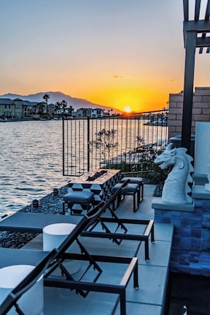 Una terrazza sul lungomare con poltrone relax, una statua decorativa a forma di drago e vista sul tramonto sull'acqua.