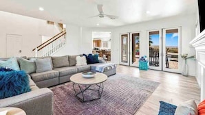 A spacious living room with a grey sectional sofa, a round coffee table, and a staircase leading to an upper floor.