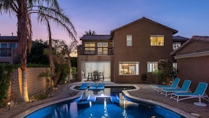 A two-story house with a swimming pool, lounge chairs, and a patio area.