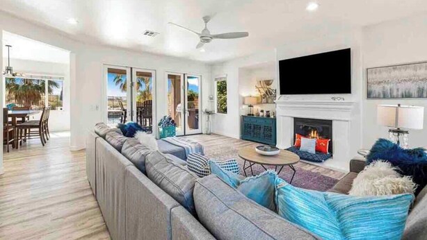 A spacious living room with a large sofa, a fireplace, a television, and a dining area with a view.