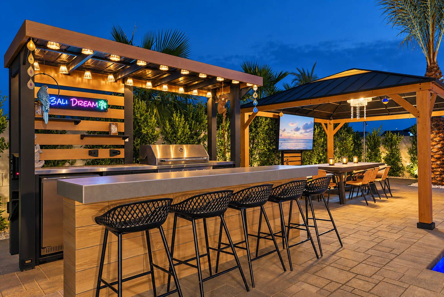 An outdoor bar area with a grill, bar stools, and a neon sign.