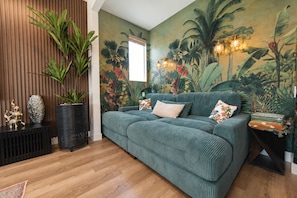 Een kamer met een groene bank, een wand van houten latten en een tropische muurschildering.