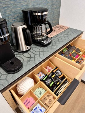 Een koffiehoek met een koffiezetapparaat, een waterkoker en een lade met koffiecups en suikerzakjes.
