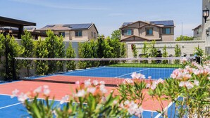 Un court de tennis en plein air, doté d’un filet, entouré de verdure et de bâtiments résidentiels.