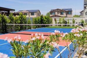 Una cancha de tenis al aire libre con red, rodeada de vegetación y edificios residenciales.