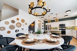 Een moderne keuken met witte kastjes, roestvrijstalen apparatuur en een eethoek met een ronde tafel voor zes personen.